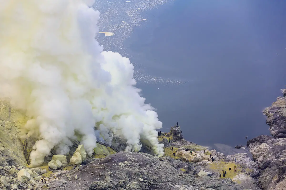 Sulfurous fumaroles of Kawah Ijen and miners of sulfur. The crater lake in the background is made acidic by similar undergound fumaroles.